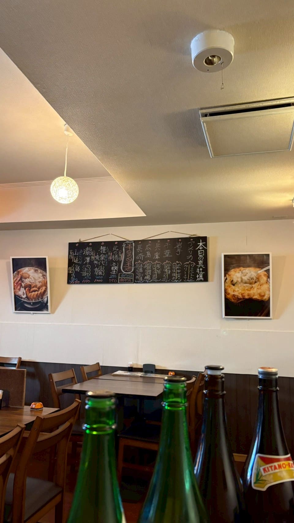 日本酒ボトル越しに見る蒲田の牡蠣居酒屋店内